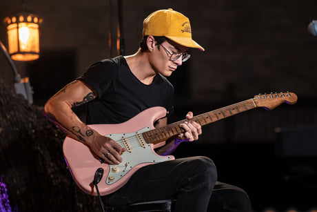 man in a yellow hat and black shirt playing a pink guitar at night